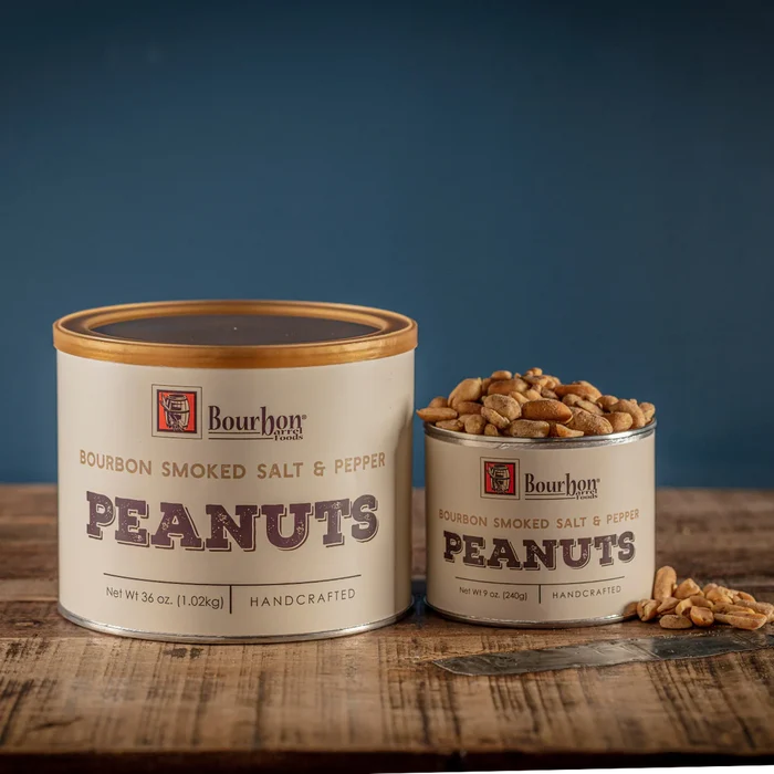 Two cans of Bourbon Smoked Salt & Pepper Peanuts on a wooden surface with a blue background.
