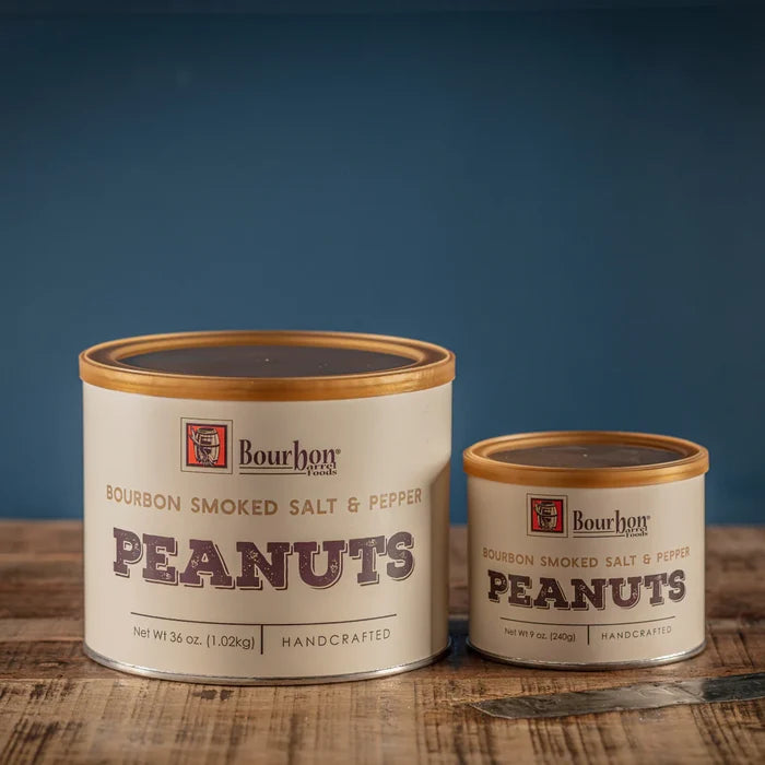 Two cans of Bourbon Smoked Salt & Pepper Peanuts by Bourhon on a wooden surface with a blue background.