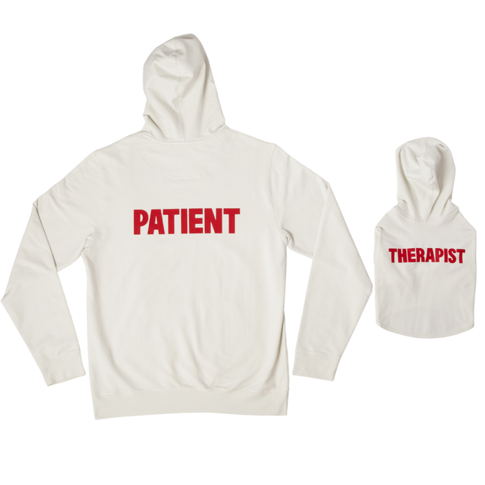 Back view of Patient Human hoodie in cream labeled PATIENT in red, shown with matching dog hoodie labeled THERAPIST on white background