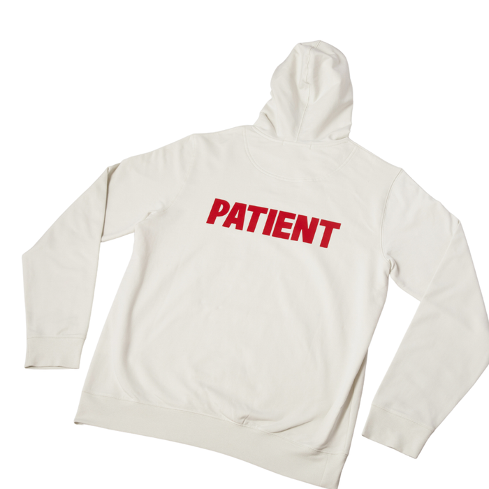 Back view of cream hoodie showcasing bold red PATIENT text on the back with white background