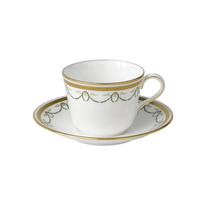 White teacup and saucer with gold and green detailing on a white background